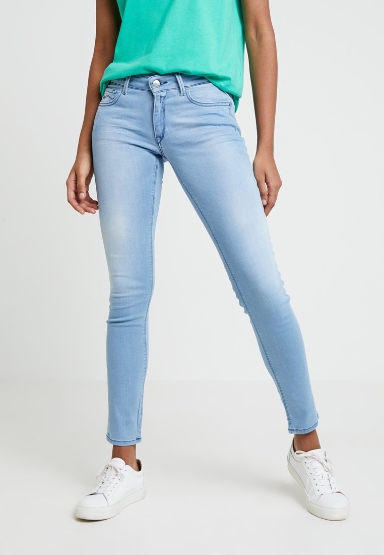 Jeans skinny de color azul claro fabricados en denim, con un diseño clásico de cuatro bolsillos, cierre de cremallera y un acabado ligeramente desgastado. Combinados con zapatillas blancas.