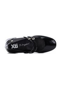 Zapato de charol negro con punta redondeada, dos hebillas de ajuste y un acabado suave y texturizado. Branding de Xti visible en el interior.