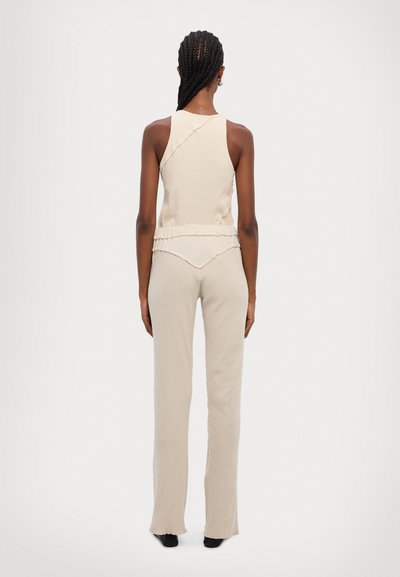 Beige ribbad toppi med asymmetrisk design, kombinerad med figurnära löspants med volangdetaljer och en lätt utsvängd nederkant.