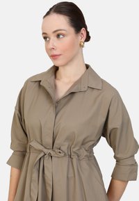 Khaki shirtjurk met een kraag, knoopsluiting aan de voorkant, taillebanddetail en opgerolde driekwartmouwen in een soepele stof.