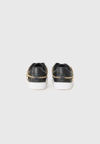 Svarte sneakers med teksturert lærfinish, hvite såler og en dekorativ gullkjedeaksent langs sidene. Merkevaren logo er preget på hælen.