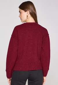 Maglione a maglia bordeaux con una vestibilità comoda, orlo a coste e leggera texture a macaroni. Presenta maniche ampie e un collo rotondo casual.