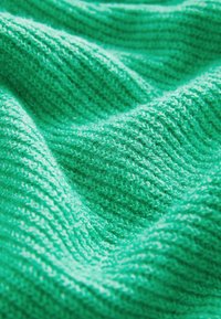 Kergeltatud kudum erksas rohelises, millel on nähtavad soonelised mustrid ja pehme, udune pind, millel on erinevad lainelised voldid.