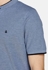 Korte mouwen polo in lichtblauwe stof met een gestructureerd patroon, voorzien van een zwart logo op de borst en een zwarte rand op de kraag.