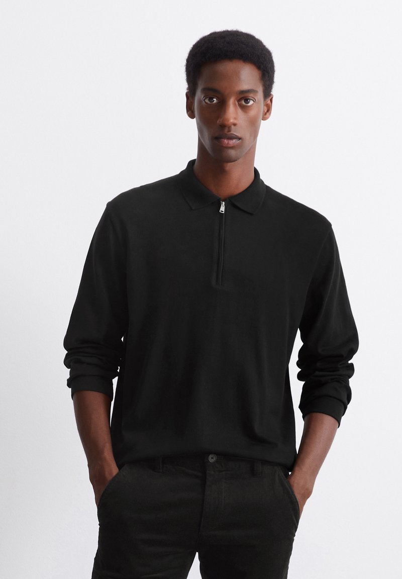 Black long-sleeve polo shirt with a zippered collar and ribbed cuffs, worn with black pants. The fabric appears smooth and soft.