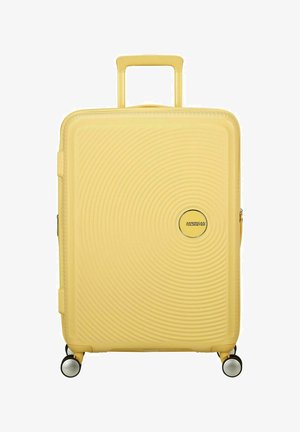 Maleta amarilla de hard-shell con un patrón circular, cuatro ruedas, un mango retráctil y un logo en la parte frontal. Cierre con cremallera.