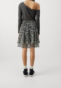 Haut gris à une épaule et à manches longues associé à une jupe noire à imprimé floral en couches. Baskets montantes noires avec semelles blanches.