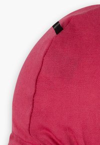Rote Stoffmütze mit runder Form, strukturiertem Material und einem kleinen schwarzen Etikett, das an die Seite genäht ist.