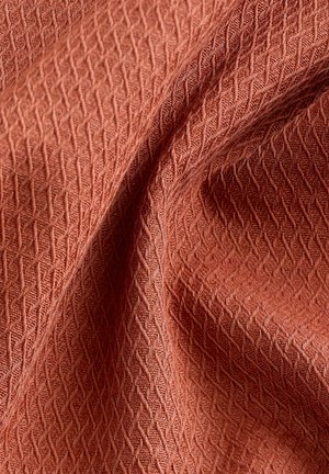 Tissu texturé de couleur rouille avec un motif géométrique, présentant une apparence douce et tissée ainsi qu'un subtil éclat. Idéal pour le rembourrage ou les vêtements.