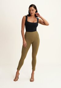 Body nero a scollo quadrato abbinato a leggings verdi oliva a vita alta. Sandali con tacco trasparente. Tessuto liscio, design aderente, senza fantasie.