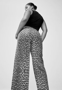 Pantalon large à imprimé léopard en noir et blanc, taille haute, en denim, avec poches arrière et finition texturée.