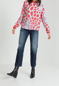 Punainen ja vaaleansininen kuviollinen pitkähihaisuus paita yhdistettynä tummansiniset suorat farkut ja mustat kiiltävät nilkkasaappaat.