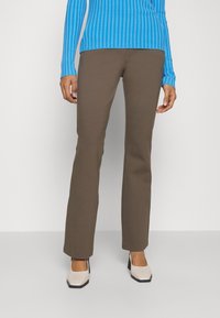 Braune, schmal zulaufende Hosen aus dehnbarem Stoff, kombiniert mit einem langärmeligen, blauen gestreiften Oberteil. Die Schuhe sind beige mit einem quadratischen Zehen-Design.