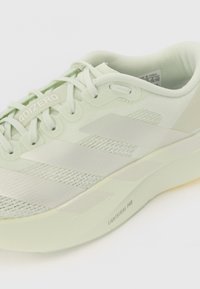 Scarpa da ginnastica verde chiaro con tomaia in rete, tre strisce bianche e dettagli riflettenti. Presenta una suola imbottita contrassegnata "LIGHTSTRIKE PRO".