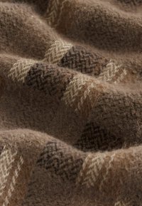 Uldtekst med et brunt og beige plaidmønster, med herringbone-detaljer. Blød tekstur med let glans og varierende farvetoner.