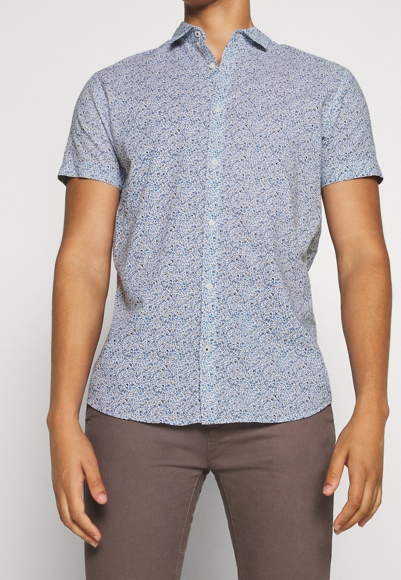 Kortärmad skjorta i ljusblått med blommönster, tillverkad av vävt material. Har en klassisk krage och knäppning fram.