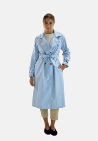 Ljusblå trenchcoat i ett mjukt material, med skärp i midjan, dubbelknäppt och med breda slag.