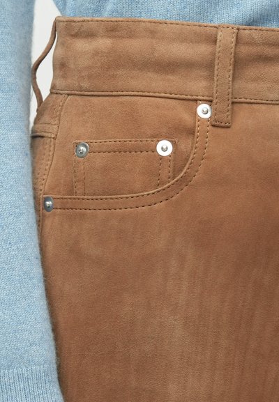 Bruine suède broek met een zijzak, zilveren accenten en zichtbare stiksels. De stof heeft een zachte textuur met een subtiele glans.