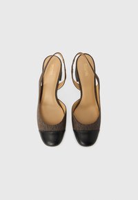 Καφέ μονογράμματα slingback flats Michael Kors με μαύρες μύτες και ταμπά εσωτερικά πέλματα σε λευκό φόντο.
