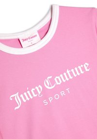 T-shirt rose clair avec encolure côtelée blanche, arborant le texte "Juicy Couture SPORT" en grande police blanche. Étiquette de taille visible.