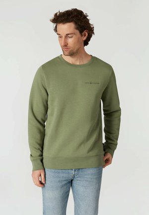 Olijfgroene sweatshirt met een ronde hals, ribgebreide manchetten en zoom. Soepele textuur met een klein logo-detail op de voorkant. Gekocht met lichtblauwe spijkerbroek.