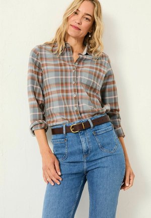 Plaid flannel shirt in gray, orange, and blue, featuring buttons and a chest pocket, paired with high-waisted blue jeans and a brown belt.