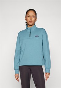 Hellblauer Fleece-Pullover mit hohem Kragen und halbem Reißverschluss, mit einem Logopatch auf der Brust und gerippten Bündchen; lockerer Schnitt.