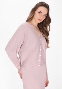 Cardigan lungo rosa con maniche a vento e scollatura a V, dotato di chiusura a bottoni sul davanti, texture morbida e vestibilità rilassata per il comfort.