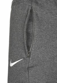 Close-up of gray fabric sweatpants showing a vertical zippered pocket and a white Nike swoosh logo below the pocket.