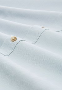 Lichtblauwe stof met een gestructureerde weving. Bevat een knoop en stikdetails langs de rand, wat een gladde, gevouwen uitstraling creëert.