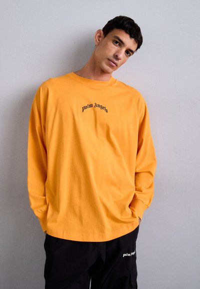 Tricou cu mânecă lungă, de culoare portocalie, din bumbac, având textul negru "palm angels" pe piept. Croiala este relaxată, cu umeri căzuți.