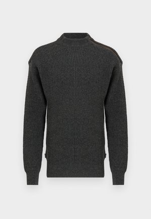 Tmavě šedý svetr s waffle pletením, vysokým límcem a zipem, který se táhne od výstřihu po jedno rameno.