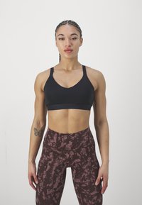 Sostenedor deportivo negro con diseño de escote en V y tirantes gruesos, combinado con leggings burdeos de cintura alta y patrón, que presentan una apariencia texturizada.