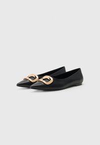 Ballerines en cuir noir avec un nez pointu et une boucle décorative dorée à l'avant. Texture lisse et design minimaliste.