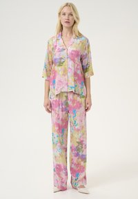 Set di abbigliamento da casa con stampa floreale realizzato in tessuto leggero. Comprende una camicia con colletto e bottoni e pantaloni a gamba larga in tonalità di rosa, giallo e blu.