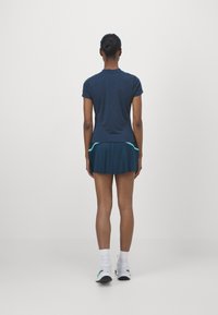 Top azul marino de manga corta combinado con una falda plisada con detalles en turquesa. El conjunto se completa con zapatos blancos y calcetines hasta la mitad de la pantorrilla.