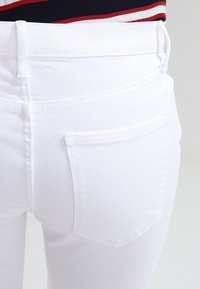 Jeans de denim blanco con un diseño ajustado, que presentan un bolsillo trasero y sutiles detalles de costura, mostrados de la cintura hacia abajo.