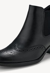 Bottine en cuir noir avec perforations brogue, panneau latéral élastique et talon bas empilé.