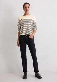 Gestreepte gebreide trui in crème en marineblauw, gecombineerd met aansluitende zwarte broek en zwarte instapschoenen. Zachte textuur en ontspannen ontwerp.