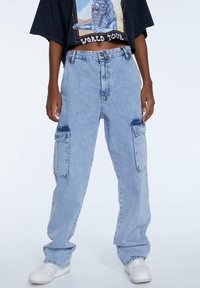 Pantalones cargo de denim en azul claro con un corte holgado, que cuentan con dos grandes bolsillos laterales y un ligero efecto de desgaste en los muslos.