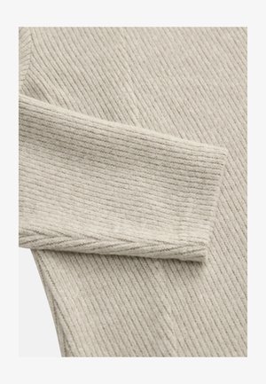 Beige ribfluweelstof met een textuur. Voorzien van een omgevouwen manchet en subtiele naaddetails, wat een eenvoudig, strak ontwerp uitstraalt.