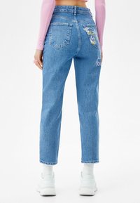 Ljust blå denimjeans med en avslappnad passform, med en fjärilsdesign på bakfickan och broderad text på baksidan.