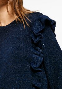 Granatowy sweter dzianinowy z błyszczącymi akcentami, z teksturowanym detalem falbany wzdłuż ramienia i klasycznym okrągłym dekoltem.