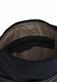Interno di una borsa in nylon blu navy con una fodera in tessuto beige che presenta sottili righe diagonali. Uno scomparto con cerniera e un'etichetta visibili all'interno.