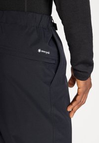 Black hiking pants made of breathable fabric feature an elastic waistband, side pocket, and a small white logo. Smooth texture with minimal seams.