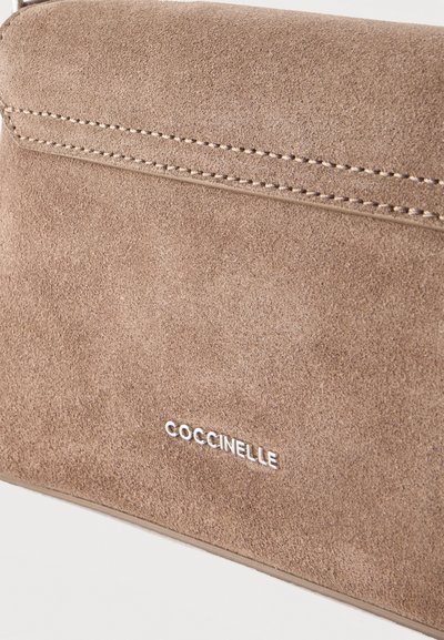 Светлокафява велурена чанта с двойни шевове и сребристо лого "Coccinelle" отпред.