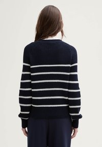 Marine-stripet genser med hvite horisontale striper, ribbete tekstur, og en avslappet passform med lange ermer og rund hals.