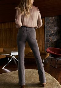 Blugi gri evazați cu talie înaltă, având buzunare la spate și o textură netedă din denim, asortați cu o bluză lungă cu mâneci lungi, ușor wrinkled.