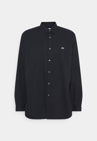 Černá košile s dlouhým rukávem na knoflíky z bavlny. Má klasický límec, stříbrné knoflíky a malé zelené logo Lacoste na hrudi.