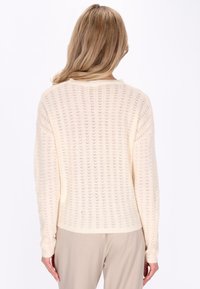 Crème kleurige gebreide trui met een losse pasvorm, geribbelde manchetten en een gestructureerd weefpatroon. Achteraanzicht toont een ronde halslijn.